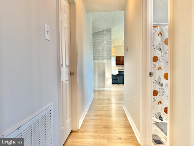 hall with a textured ceiling, baseboards, and light wood-type flooring