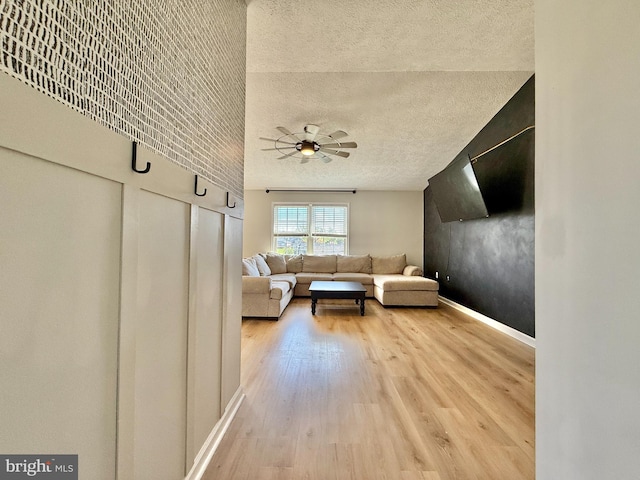 living area featuring baseboards, a ceiling fan, light wood-style floors, and a textured ceiling