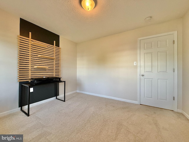 empty room featuring a textured ceiling, carpet flooring, and baseboards