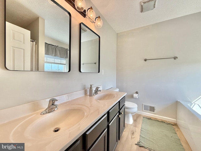full bath featuring wood finished floors, toilet, a sink, visible vents, and a textured ceiling