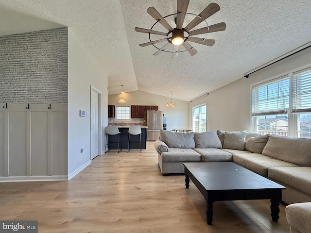 living area with ceiling fan, light wood-style floors, a textured ceiling, and vaulted ceiling