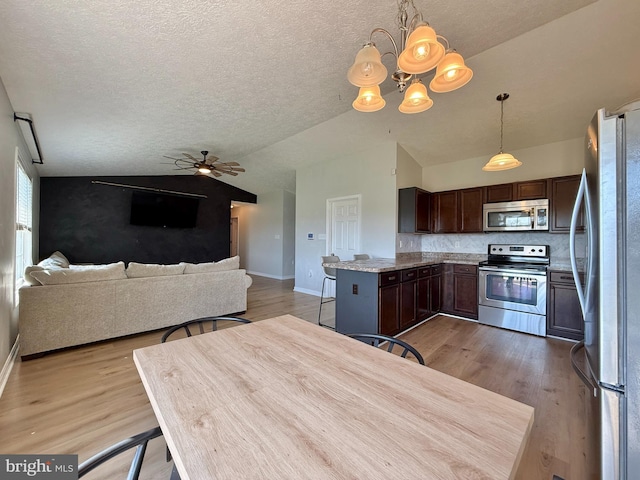 kitchen with appliances with stainless steel finishes, light wood finished floors, vaulted ceiling, and baseboards