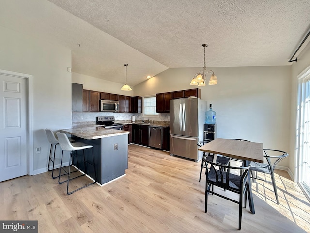 kitchen with a chandelier, stainless steel appliances, dark brown cabinets, light wood finished floors, and a peninsula