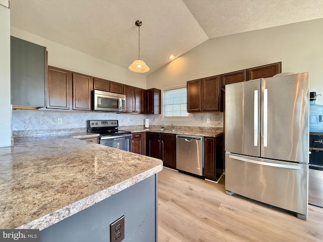 kitchen with pendant lighting, stainless steel appliances, dark brown cabinetry, light wood finished floors, and vaulted ceiling