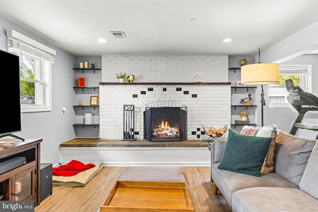 living room featuring visible vents, a brick fireplace, wood finished floors, and a healthy amount of sunlight