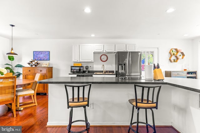 kitchen featuring stainless steel fridge, a breakfast bar, a sink, and white cabinetry