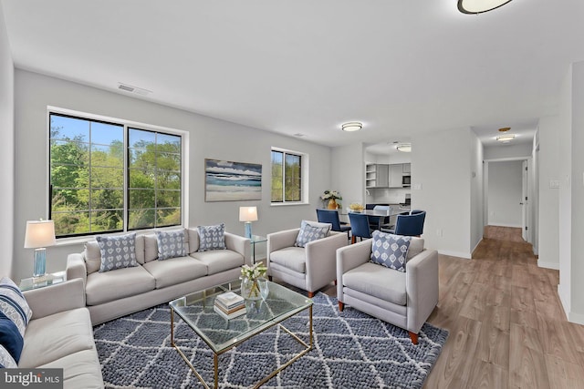 living area featuring visible vents, light wood-style flooring, and baseboards