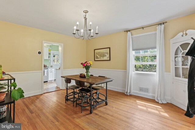 dining room featuring visible vents, light wood-style floors, a wainscoted wall, and a notable chandelier