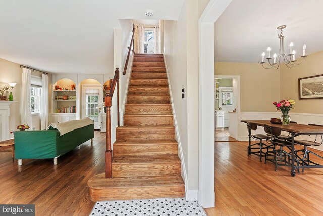 stairs with a chandelier, wood finished floors, and a wealth of natural light