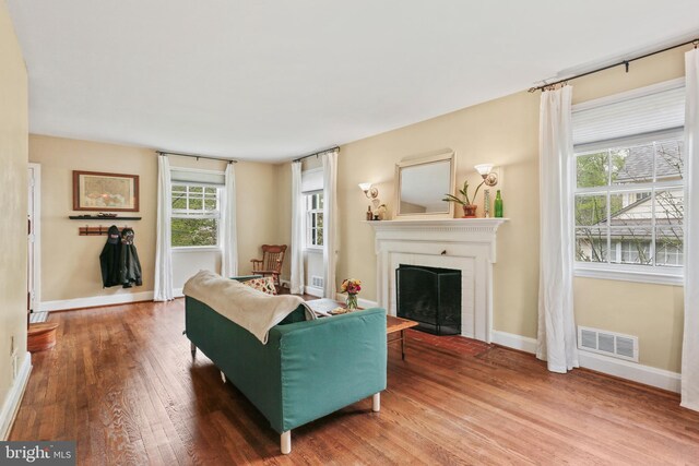 living area featuring baseboards, a fireplace with flush hearth, wood finished floors, and visible vents