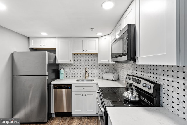 kitchen with a sink, white cabinets, dark wood-style flooring, appliances with stainless steel finishes, and decorative backsplash