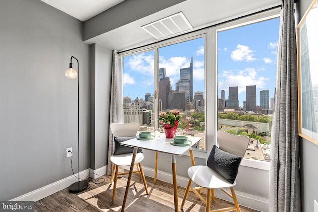 dining area with a city view, baseboards, visible vents, and wood finished floors