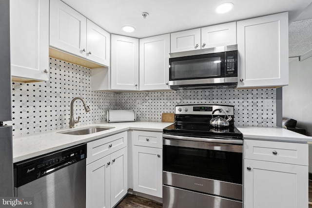 kitchen with a sink, white cabinetry, backsplash, light countertops, and appliances with stainless steel finishes