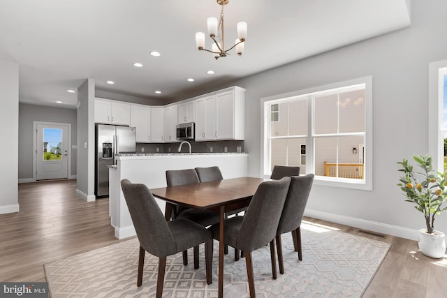 dining area with visible vents, light wood-style flooring, baseboards, and an inviting chandelier