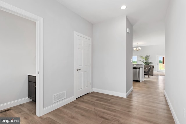 corridor with an inviting chandelier, baseboards, wood finished floors, and visible vents