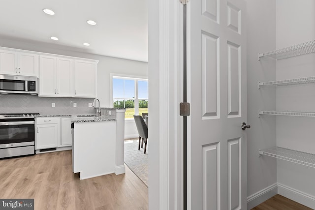 kitchen with a sink, white cabinets, stainless steel appliances, and light wood-style flooring