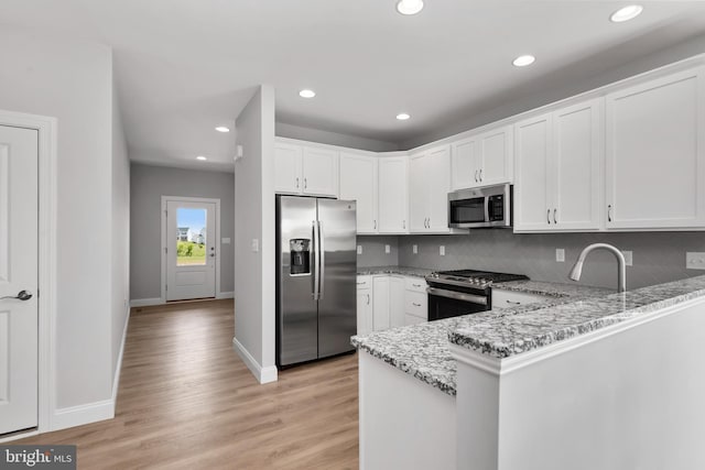 kitchen featuring light stone counters, baseboards, a peninsula, stainless steel appliances, and white cabinetry
