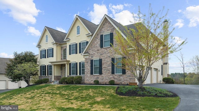 craftsman-style house with aphalt driveway, a garage, stone siding, stucco siding, and a front yard