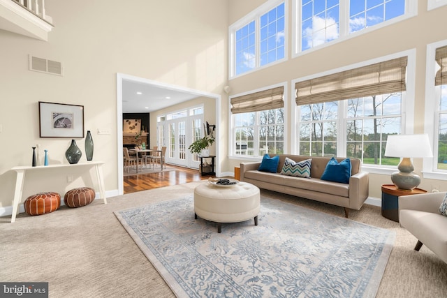 carpeted living room featuring a healthy amount of sunlight, baseboards, a high ceiling, and visible vents
