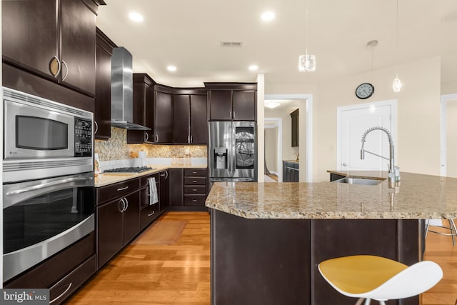 kitchen with wall chimney range hood, a sink, light wood-style flooring, stainless steel appliances, and visible vents