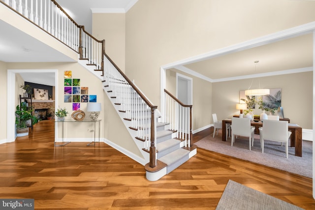 stairs with crown molding, a fireplace, wood finished floors, baseboards, and a high ceiling