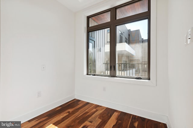 spare room with baseboards and dark wood-type flooring