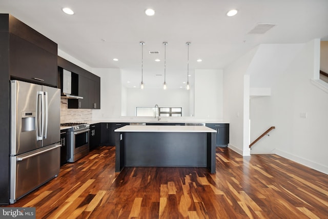 kitchen with stainless steel appliances, light countertops, wall chimney range hood, a sink, and a center island