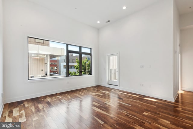 spare room featuring wood finished floors, a high ceiling, baseboards, and recessed lighting