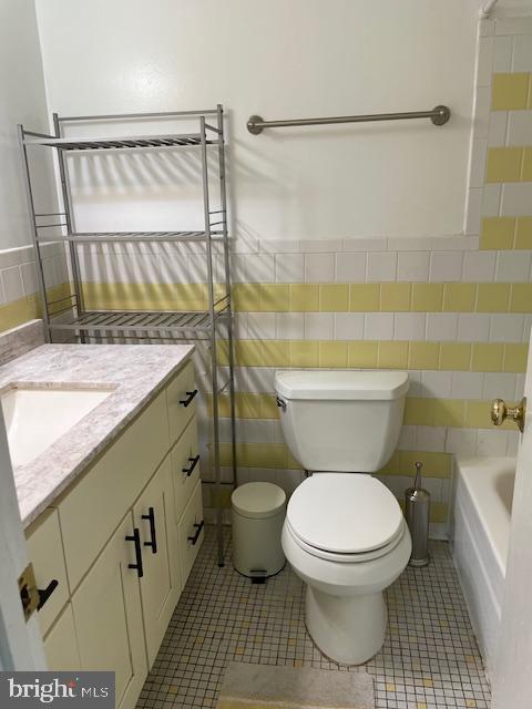 full bathroom with a bath, tile walls, tile patterned floors, vanity, and toilet