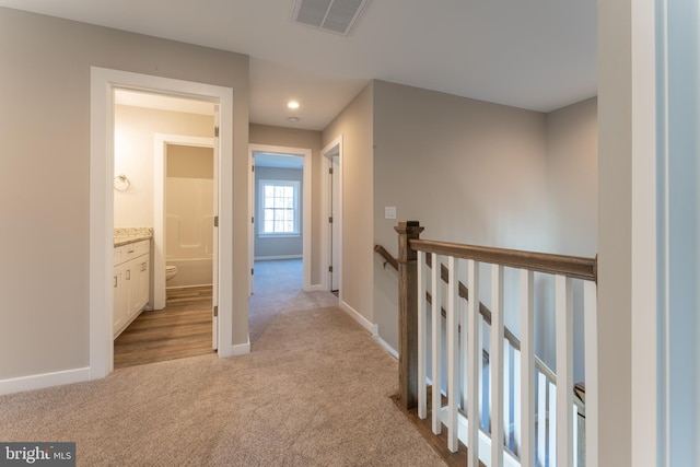 corridor featuring light colored carpet, baseboards, visible vents, and an upstairs landing