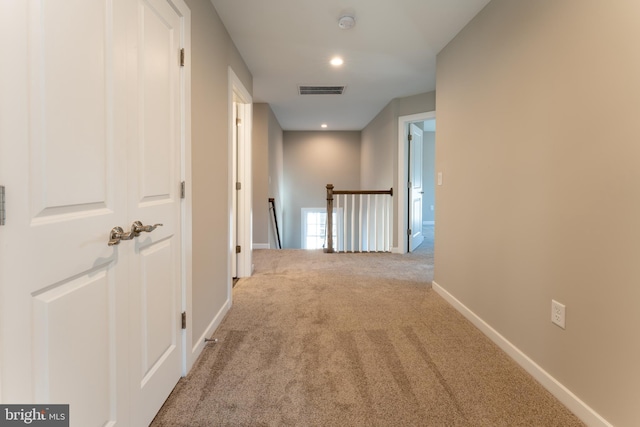 hallway featuring baseboards, carpet, visible vents, and an upstairs landing