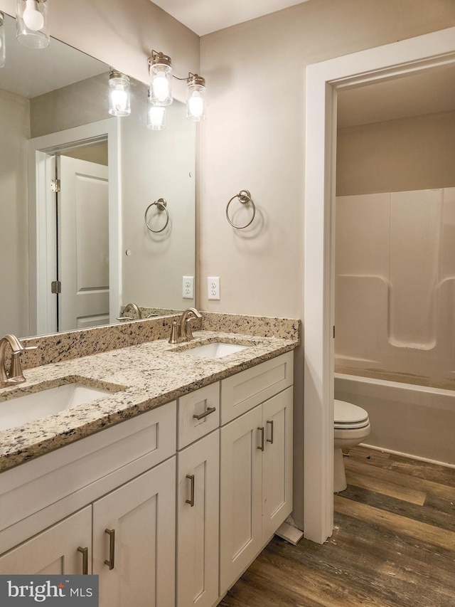 full bath featuring double vanity, a sink, wood finished floors, and toilet