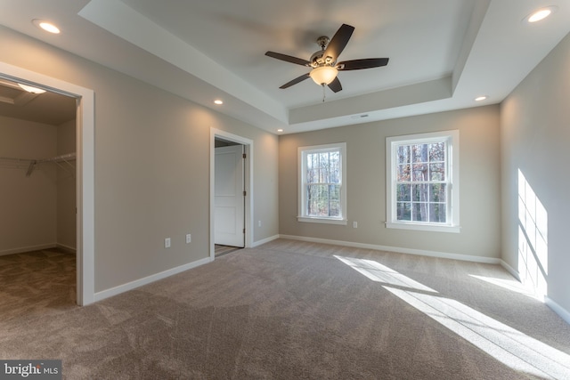 unfurnished bedroom with baseboards, a spacious closet, carpet, a tray ceiling, and recessed lighting