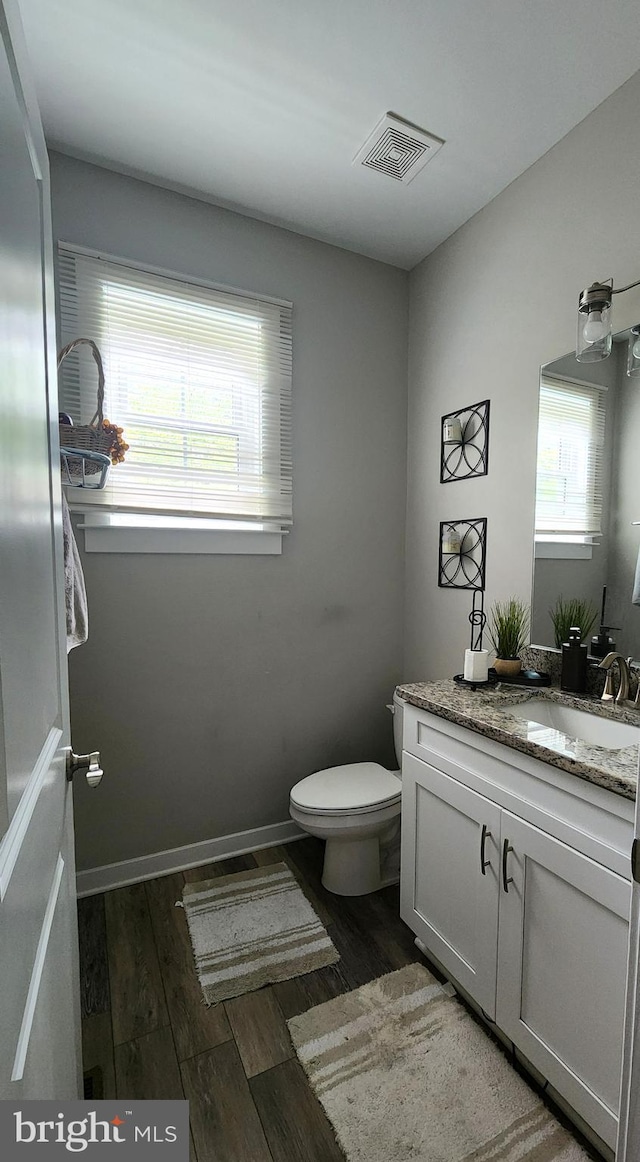 half bath featuring vanity, toilet, a wealth of natural light, wood finished floors, and visible vents
