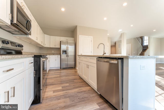 kitchen featuring stainless steel appliances, white cabinetry, and light wood-style flooring