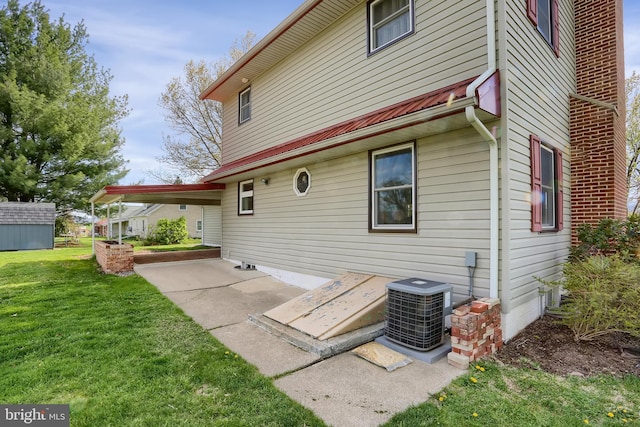 rear view of property featuring central air condition unit, a carport, and a lawn