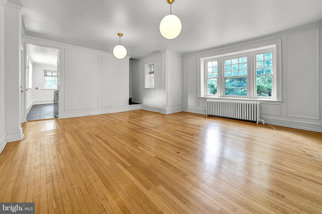 unfurnished living room featuring radiator, light wood finished floors, a decorative wall, crown molding, and baseboards
