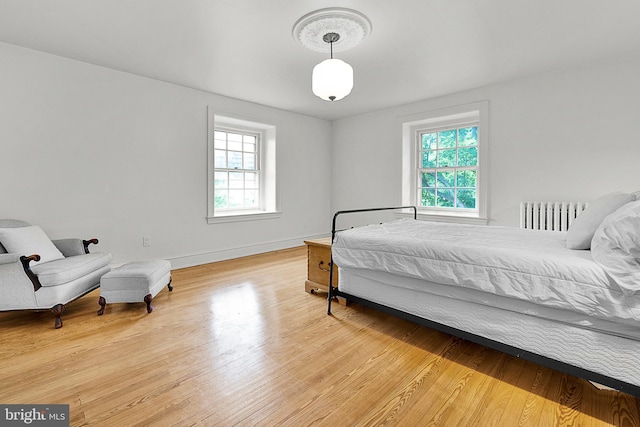 bedroom with light wood-type flooring, baseboards, and radiator heating unit