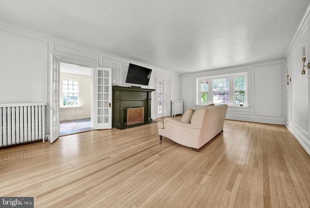 living area with radiator heating unit, a decorative wall, radiator, light wood-style floors, and crown molding