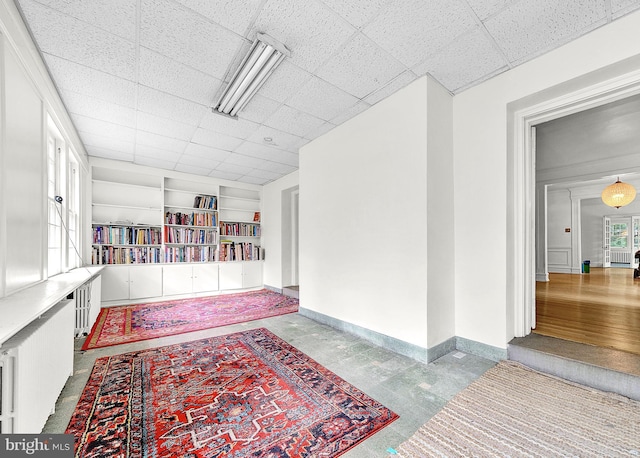 hallway with built in shelves, baseboards, and a paneled ceiling