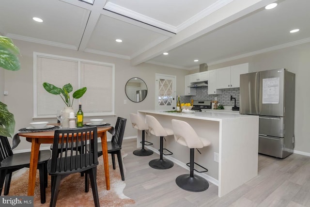 kitchen featuring light wood finished floors, baseboards, light countertops, under cabinet range hood, and appliances with stainless steel finishes