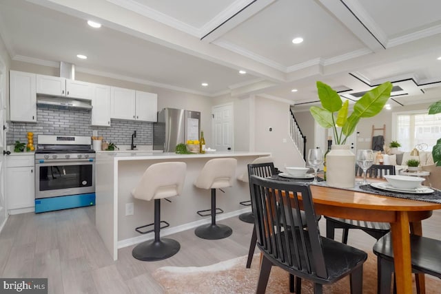 kitchen with a breakfast bar area, light wood-type flooring, appliances with stainless steel finishes, white cabinetry, and under cabinet range hood