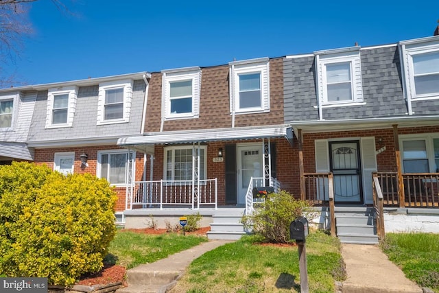 townhome / multi-family property with brick siding, roof with shingles, a porch, and mansard roof