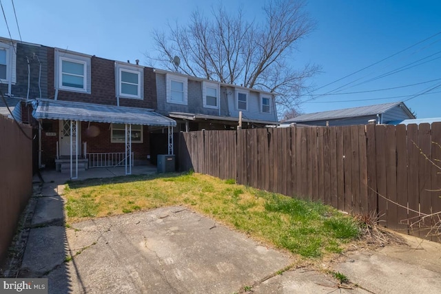 rear view of house featuring brick siding, mansard roof, central AC, and fence