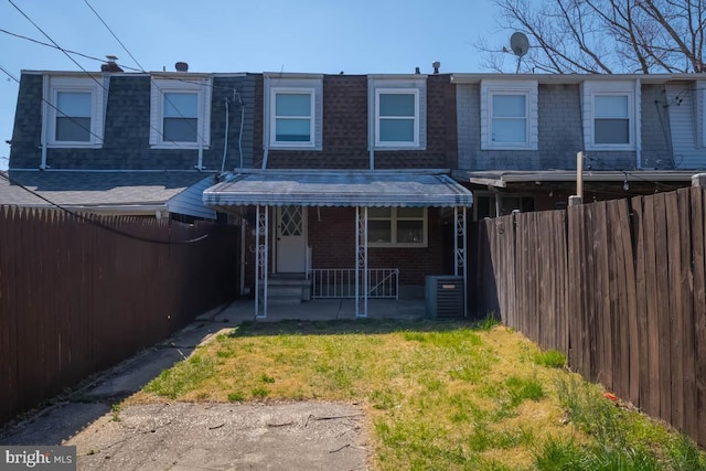 back of house with a fenced backyard, a shingled roof, brick siding, and mansard roof