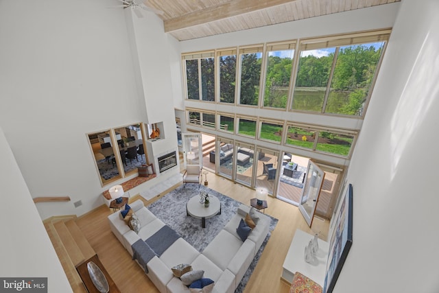 living room featuring beamed ceiling, a towering ceiling, wood finished floors, and a glass covered fireplace