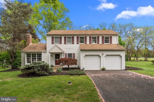 traditional-style home with a chimney, aphalt driveway, an attached garage, roof with shingles, and a front lawn