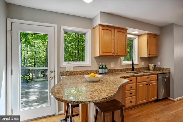 kitchen featuring stainless steel dishwasher, light stone countertops, a kitchen breakfast bar, a sink, and light wood finished floors