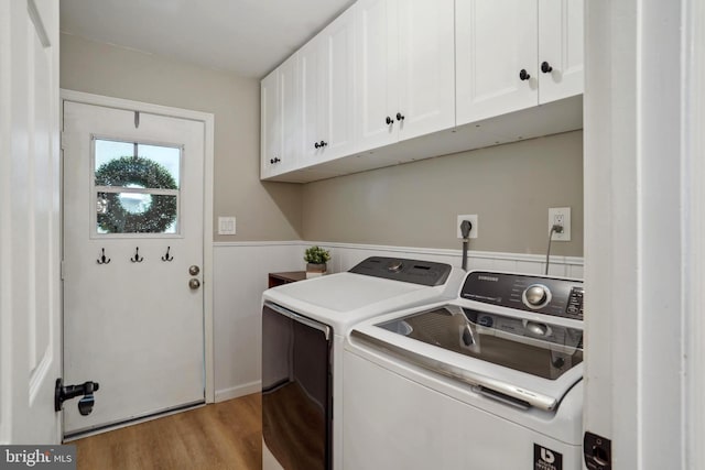 laundry area featuring light wood-type flooring, washer and clothes dryer, cabinet space, and a wainscoted wall