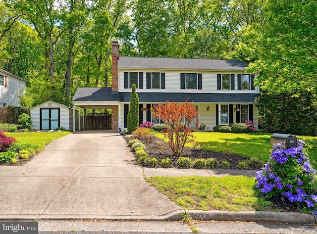 traditional home featuring a front yard, driveway, a chimney, a storage unit, and an outbuilding